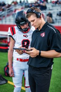 Public school coach housing assistance programs; photo of coach on field with football player looking at tablet. 